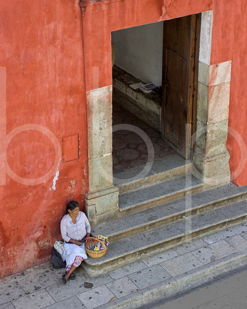 A peasant woman who is a street vendor sits on the step by a doorway with an apron and her basket of candy for sale In This Commercial Environmental Portrait Photograph By Brian Buckner Photography.