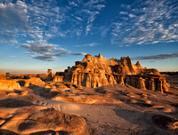 A beautiful sandstone formation in the bisti/de-na-zin wilderness area that looks like a castle made of clay and rock is illuminated by the rays of the dawning sun under a blue sky with striated cloud