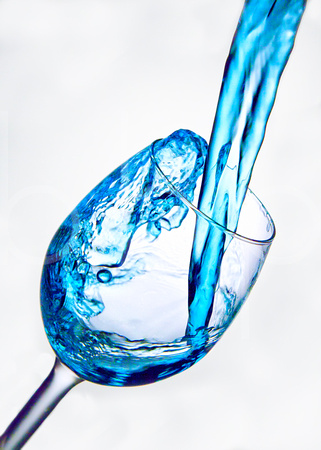Beautiful Blue Colored liquid is captured in motion as it is poured into a wine glass against a white back drop in a photography studio environment.