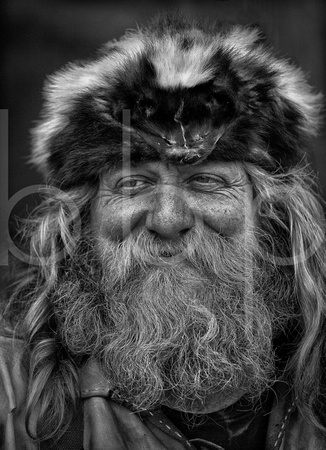 A Smiling Frontier Rendezvous Mountain Man Dressed In Buckskins And Sporting A Hat Made From A Skunk Skin In This In This Black And White Commercial Environmental Portrait By Brian Buckner Photography