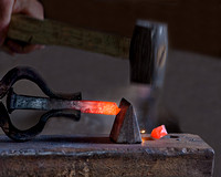 A blacksmith's hammer strikes and cuts through hot glowing iron on the anvil in a forge in this commercial environmental industrial photograph by Brian Buckner Photography, Shreveport, Louisiana.