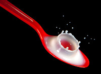 A drop of milk impacts a red spoon filled with more milk creating a corona or crown like splash in this commercial product photograph by Brian Buckner Photography, Studio "B", Shreveport, Louisiana.