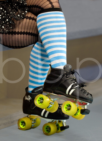 A roller derby girl's fishnet hose and blue striped socks clad her powerful legs and black and yellow skates are on her feet.