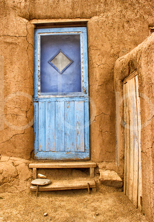 At a pueblo structure in taos a faded blue door is in contrast to the yellow brown adobe pueblo dwelling it serves.