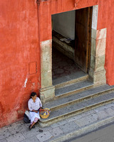 A peasant woman who is a street vendor sits on the step by a doorway with an apron and her basket of candy for sale In This Commercial Environmental Portrait Photograph By Brian Buckner Photography.