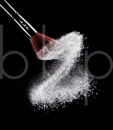 A Woman's Cosmetic Powder Brush Is Shown In Motion As It Delivers A Beautiful "S" Curve of Powder in this commercial product photograph by Brian Buckner Photography, Studio "B", Shreveport, Louisiana.
