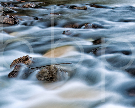 Beautiful rushing creek water dashs past exposed rocks that support a lone twig in this commercial landscape photograph by Brian Buckner Photography, Shreveport, Louisiana.