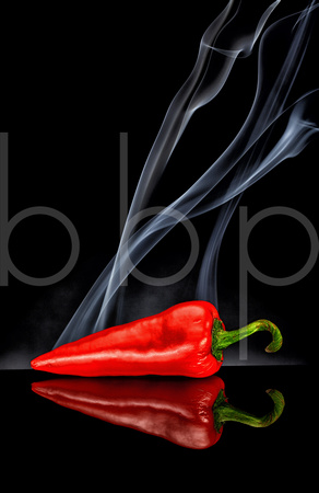 A Smoking Hot Red Pepper is shown on a beautiful black reflective surface as smoke rises from it suggesting firey heat in this commercial product photograph by brian buckner photography.