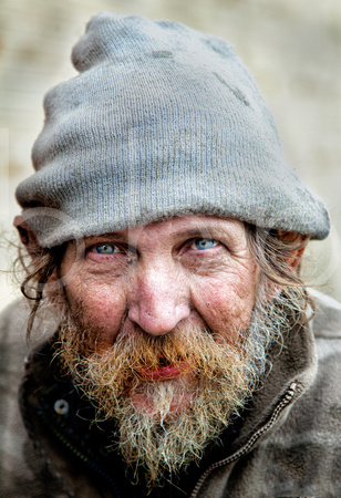Ricky is a white homeless man wearing a stocking hat and an old green jacket with a heavy grey beard In This Compelling Environmental Portrait or Street Photograph By Brian Buckner Photography.